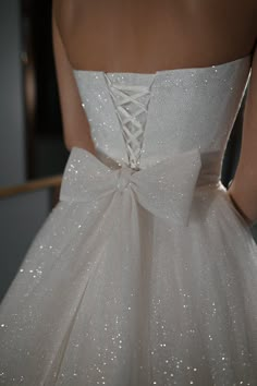 the back of a white wedding dress with sequins on it and a bow at the waist