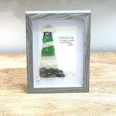 a shadow frame with a green and white lighthouse in it on top of a wooden table