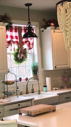 a kitchen with white cabinets and an island in front of a window that has christmas decorations hanging from it