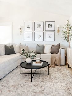 a living room with white couches and pictures on the wall above it's coffee table