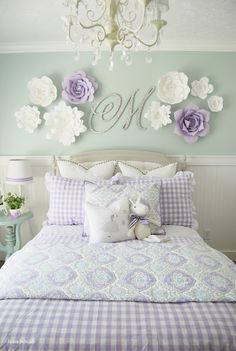 a bed with purple and white flowers on the wall above it, next to a chandelier