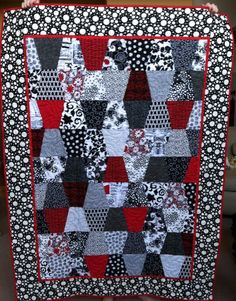 a black and white quilt with red trim on the edges is being held up by a person