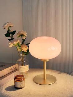 a table with a lamp, jar and flowers on it next to a stack of books