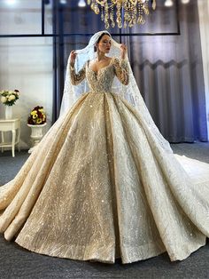 a woman in a gold wedding gown standing next to a chandelier with lights hanging from it