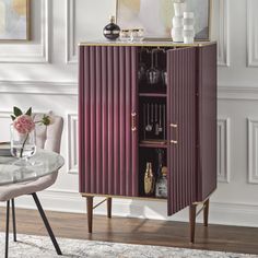 a purple cabinet with wine glasses on it in front of a white wall and rug