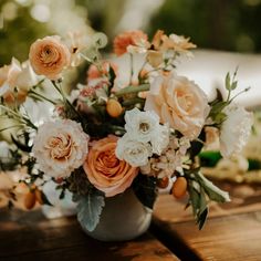 a vase filled with lots of flowers sitting on top of a wooden table covered in greenery