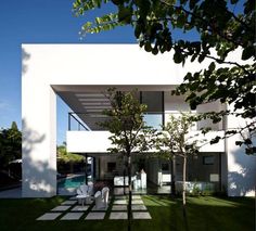 a white house with grass and trees in the front yard, next to a swimming pool