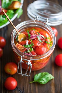 a jar filled with tomatoes and onions on top of a wooden table next to other vegetables