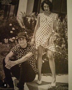 a man kneeling down next to a woman in a polka dot dress and hat on the sidewalk