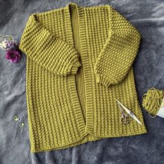 a yellow knitted sweater next to some scissors and yarn on a gray surface with flowers