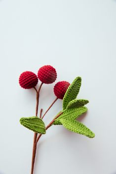 three red flowers with green leaves on a white surface, one is crocheted and the other is knitted