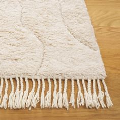 a white rug with fringes on top of a wooden floor