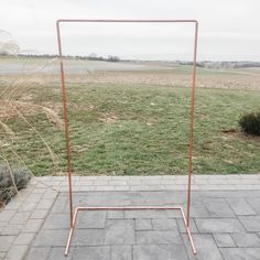 a metal frame stands in the middle of a field with grass and bushes behind it