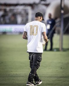 a man in white shirt and black pants walking on field with baseball bat behind him