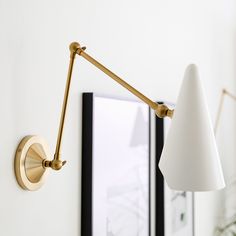 a wall light with a white shade on it's arm next to a mirror