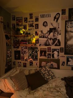 an unmade bed with lots of posters on the wall above it and a lamp next to it