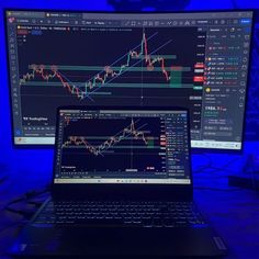 a laptop computer sitting on top of a desk next to a monitor with an image of a stock chart