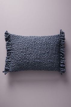 a blue pillow with tassels on the front and back, against a purple wall