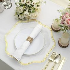 a table set with white and gold plates, silverware, flowers and napkins