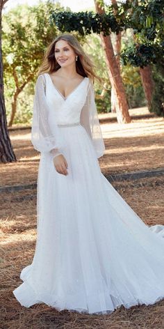 a woman in a white wedding dress posing for the camera with trees in the background