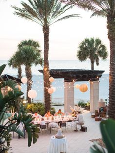 an outdoor dining area with palm trees and lights strung from the ceiling, overlooking the ocean