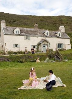 two people sitting on a blanket in front of a house