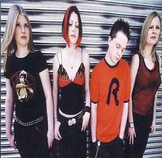 three women and one man standing in front of a garage door with their eyes closed