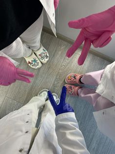 three people in white coats and pink gloves standing around each other with their hands on the floor