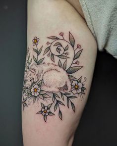 a tattoo with flowers and a sleeping animal on it's thigh, done by the artist