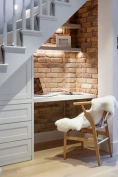 a white chair sitting under a stair case next to a desk and bookshelf