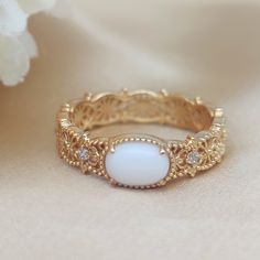 a close up of a ring on a white cloth with flowers in the back ground