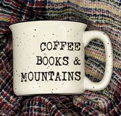 a coffee mug that says coffee books and mountains on it sitting on a plaid blanket