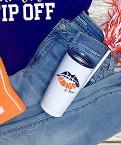 a pair of jeans, an orange and white frisbee, and a blue t - shirt are sitting on a wooden surface