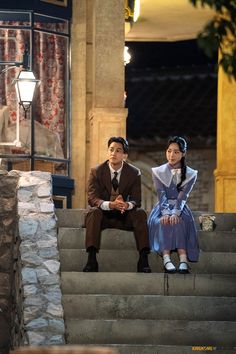 two people sitting on some steps in front of a building