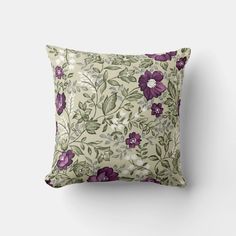 a pillow with purple flowers and green leaves on the front, sitting against a white wall