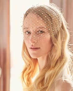 a woman with long blonde hair wearing a birdcage veil over her head and looking off to the side