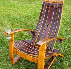 a wooden lawn chair sitting in the grass with a glass of wine next to it