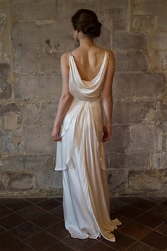 a woman in a white dress standing against a stone wall with her back to the camera