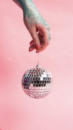 a person's hand holding a disco ball ornament on a pink background