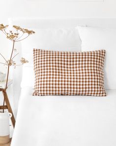 a brown and white gingham pillow sitting on top of a bed next to a vase with flowers