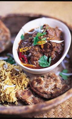 a wooden bowl filled with meat and rice next to some pita bread on a plate