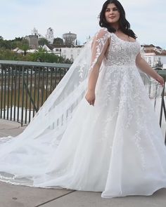 a woman in a white wedding dress standing on a bridge wearing a long veil over her shoulder