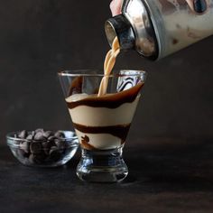 someone pouring chocolate into a dessert in a small glass cup with coffee beans on the side