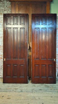 two large wooden doors sitting next to each other in front of a brick wall and floor