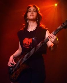 a woman holding a guitar in her right hand and looking up at the sky with red lights behind her