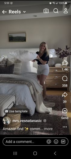 a woman standing in front of a bed with pillows and blankets on top of it