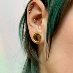 a woman with green hair wearing an ear cuff and gold plated piercings on her ears