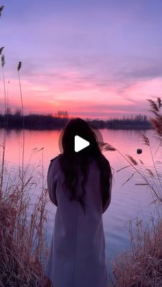 a woman standing in front of a body of water at sunset