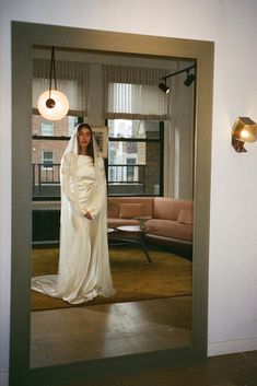 a woman in a white wedding dress is standing in front of a mirror with her hands on her hips