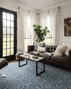 a living room filled with furniture and a large window covered in white drapes next to a blue rug